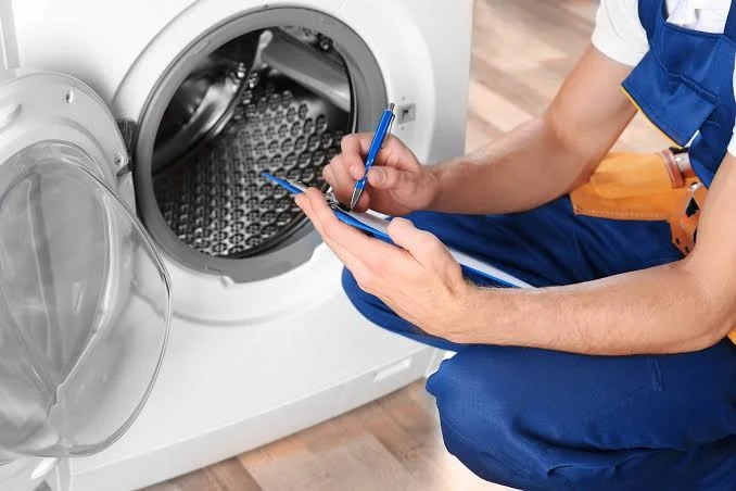 Technician taking diagnostic notes beside an open laundry appliance