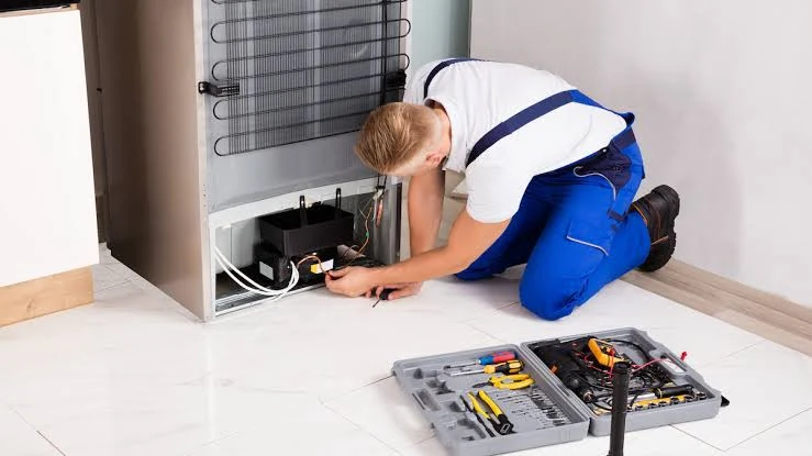 Technician servicing components at the back of a refrigerator