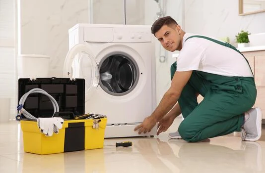 Technician inspecting a front-loading washing machine beside a yellow toolbox